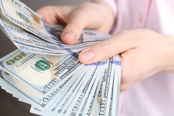 Woman counting dollar banknotes on light grey background, closeup