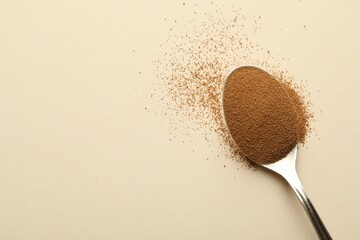 Spoon with instant coffee on beige background, top view. Space for text