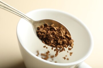 Putting instant coffee into cup on beige background, closeup