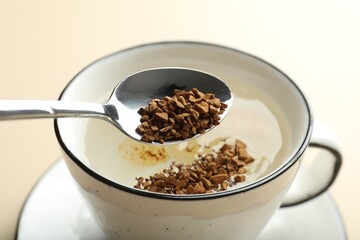 Putting instant coffee into cup on beige background, closeup