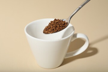 Putting instant coffee into cup on beige background, closeup