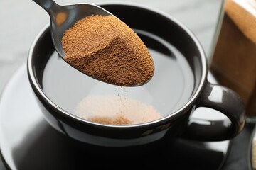 Putting instant coffee into cup at table, closeup
