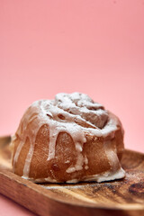 Cinnamon roll with icing on wooden platter against pink background