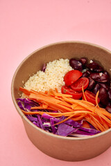 Colorful vegan salad bowl with quinoa tomatoes beans carrots cabbage on pink background