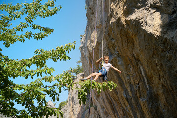 Brave boy suspended on a rope, rock climbing outdoors. Dynamic shot of adventure, challenge, and...