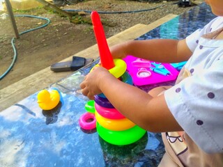 A child is busy stacking colorful rings onto a cone-shaped base, a classic toy, on a shiny surface,...