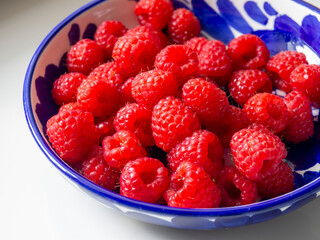 Red raspberries in a blue bowl on the table. Raspberry season. Local garden berry offer