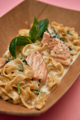 Creamy salmon fettuccine with basil on a brown plate against pink background