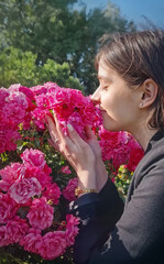 Lovely young woman enjoys the presence in the rose garden as enjoys smelling a large cluster of vibrant pink rosy, savouring the fragrance with closed eyes, gently touching the blooms