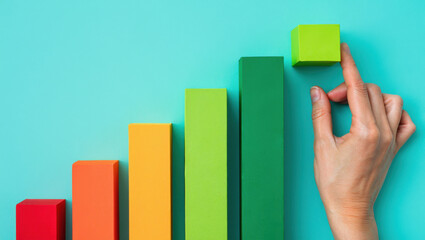 Building Towards Success A Hand Placing a Block Atop a Growing Bar Graph on a Teal Backdrop Symbolizing Progress and Achievement in Business and Development