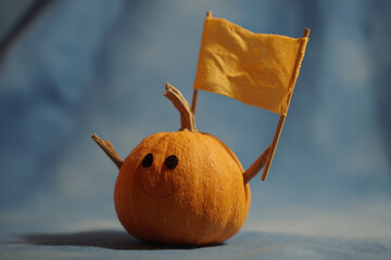 Cheerful pumpkin with tiny handmade flag on blue background