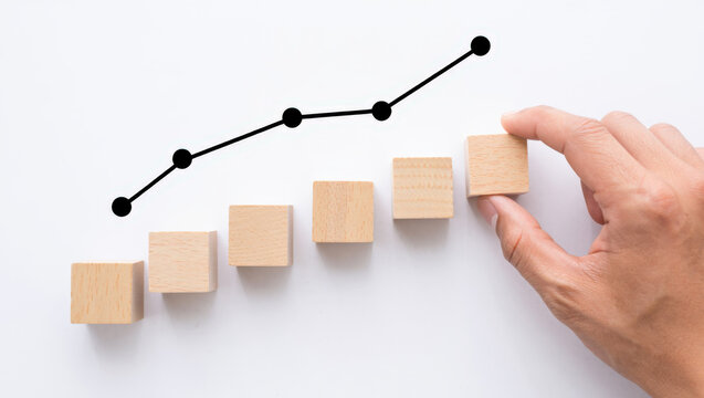 Building Success A Hand Adding a Wooden Block to an Ascending Bar Graph with an Upward Trending Line Illustrating Growth and Achievement on a White Background