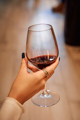 Elegant hand holding wine glass with red wine in cozy setting reflecting warm atmosphere