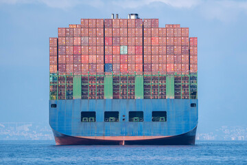 Big enormous container ship on the sea in front of the coast and harbor entrance, back view from...