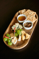Gourmet cheese platter with crackers and honey on wooden tray