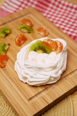 Delicious pavlova topped with fresh kiwi and mandarin on wooden board