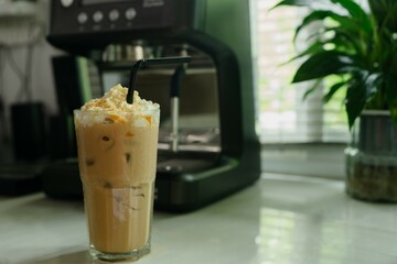 caramel latte with whipped cream resting by the kitchen window beside a flower pot sweet caffeine in calm morning at home.