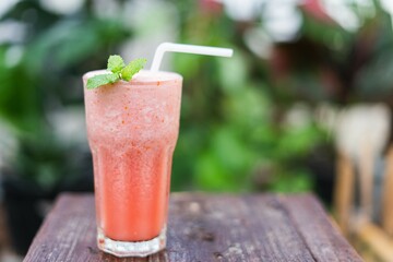 refreshing watermelon smoothie with mint leaves on wooden table in a lush garden, healthy delicious drink in one summer moment.