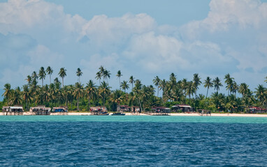 Malaysia. A view of the shore of a reef island with coconut palms and the huts of a sea gypsy village near the town of Semporn on the island of Borneo.