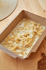 Creamy fettuccine pasta in cardboard container on wooden table surface