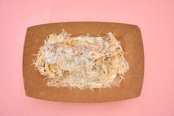 Creamy truffle pasta with shredded parmesan in eco-friendly brown tray on pink background