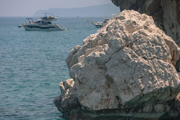 Yacht holidays in the Mediterranean Sea. In the sea, near the rocks, people relax on yachts. A sea boat is visible next to the rock. In summer, people relax on a yacht in the sea next to large rocks.