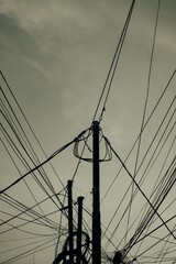 Silhouettes of electric utility poles and tangled overhead wires against cloudy sky