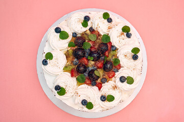 Delicious pavlova with mixed berries on pink background with whipped cream and mint leaves