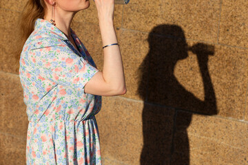 Woman drink water from the bottle on a street, shadow on stone wall. Concept of thirst, hot weather...