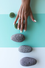 Woman's hand with mint green nails reaching for gray stones on a colored background