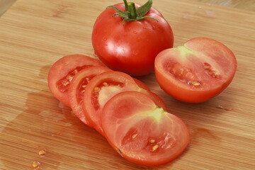 Ripe tomatoes are placed on the table with cut tomatoes.