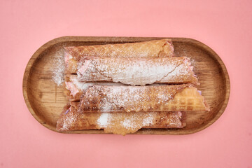 Delicious strawberry waffle rolls with powdered sugar on wooden platter