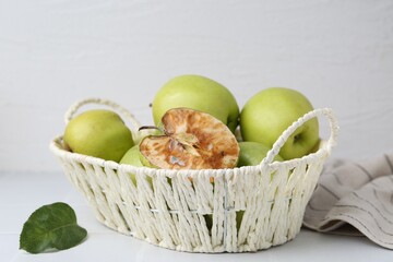 Spoiled apple and good ones in basket on white table