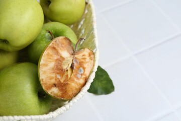 Spoiled apple and good ones in basket on white table, closeup. Space for text