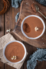 Creamy chocolate mousse in a white bowl, elegantly presented on a wooden board with a silver spoon...