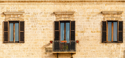 old yellow facade of house with three brown vintage wooden windows in retro italian european style
