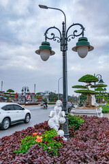 A bustling city street showcases ornamental street lamps and carefully trimmed plants amidst...