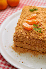 Close-up of honey cake with crumbled topping and tangerine slices on white plate