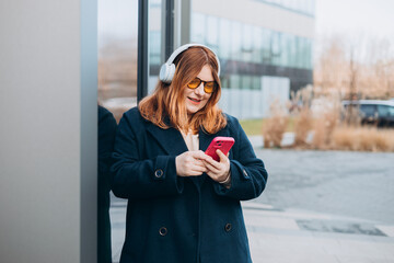 30s millennial Caucasian lady student in wireless headphones with phone listen music, enjoy audio...