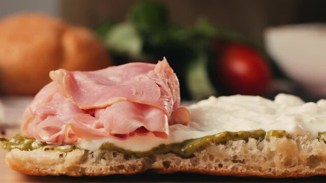 Mortadella ham sandwich, Traditional italian focaccia filled with thin pesto slices of mortadella, served by chef man in cafe restaurant. Macro of traditional italian spanish tapas antipasti. 