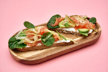 Smoked salmon and avocado toast on wooden board with spinach and fennel on pink background