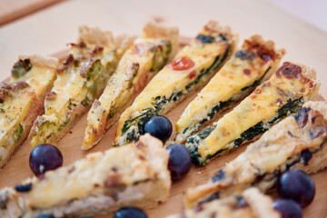 Delicious slices of quiche with spinach and tomato on wooden platter with grapes