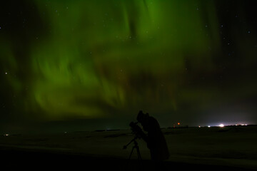 person under night aurora sky with telescope