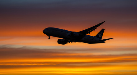 Silhouette of a large passenger airplane in flight against a vibrant sunset backdrop. The image captures the drama of air travel and the beauty of the twilight sky.