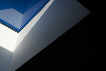 Triangular white ceiling forming skylight, framing blue sky through clear glass in vaulted hall