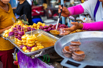 A street vendor prepares Thai sweets including fried bananas and purple yams, offering a taste of local cuisine
