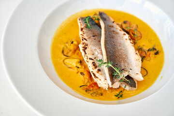 Grilled trout on curried mussel sauce with thyme garnish in white bowl