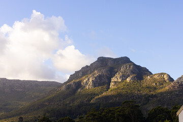 Rocky mountain peak shining under sun with shrub terraces and white clouds drifting across blue sky