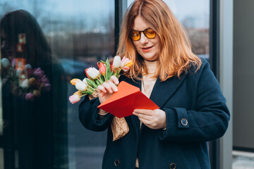 Portrait of nice attractive lovely pretty cheerful woman getting receiving congrats card greetings and big bouquet flowers, outdoors