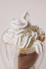 Whipped cream is squeezed out of a can onto a rotating cup of coffee on a white